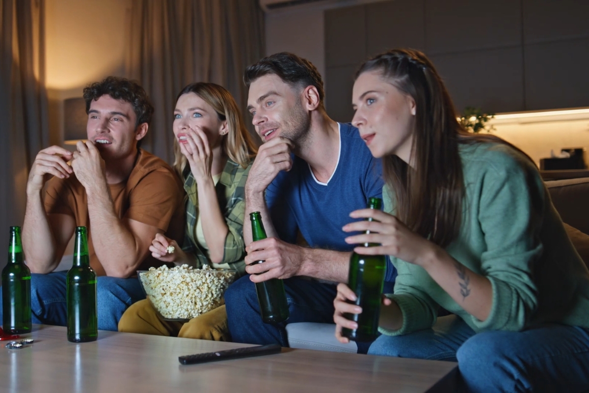 grupa priajtelja, dve devojke i dva muškarca grickaju kokice i piju pivo dok gledaju seriju