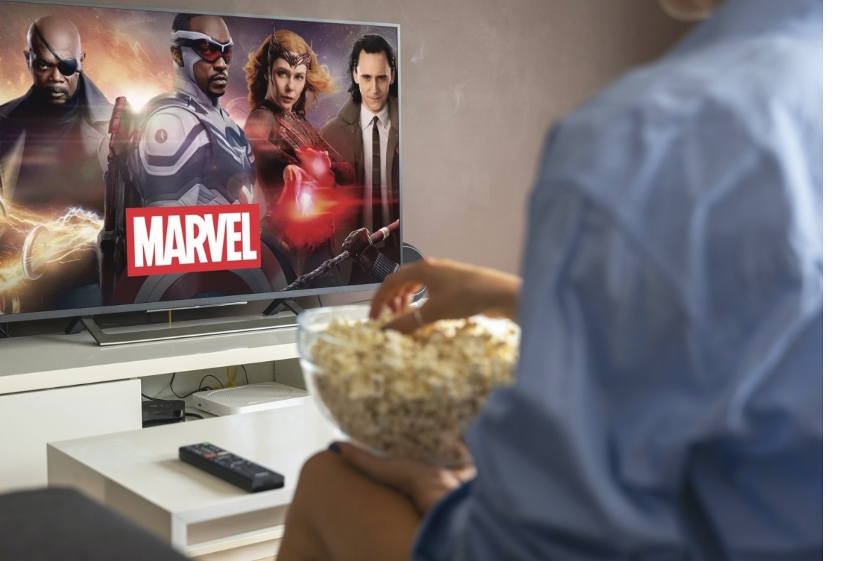 osoba gleda marvel film na televizoru i drži činiju sa kokicama u rukama